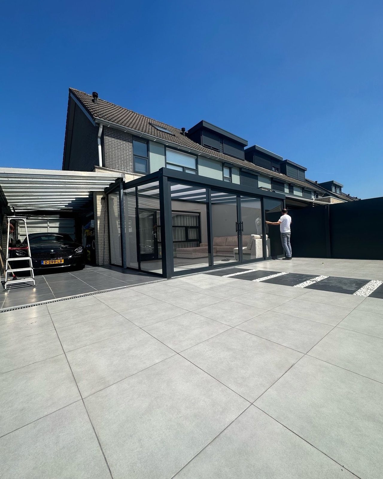 Tuinkamer met glazen schuifwanden naast de garage, met een groot tegelterras