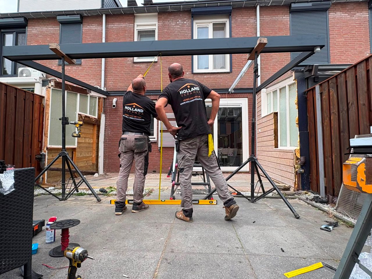 Twee monteurs in Holland Veranda-shirts stellen een frame waterpas af