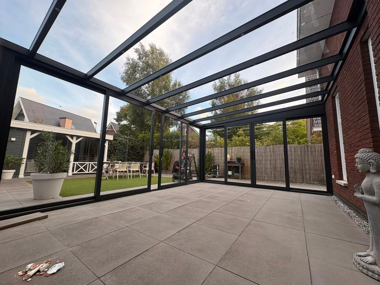 Zicht vanuit een veranda met glazen dak en glazen schuifwanden rondom op de tuin
