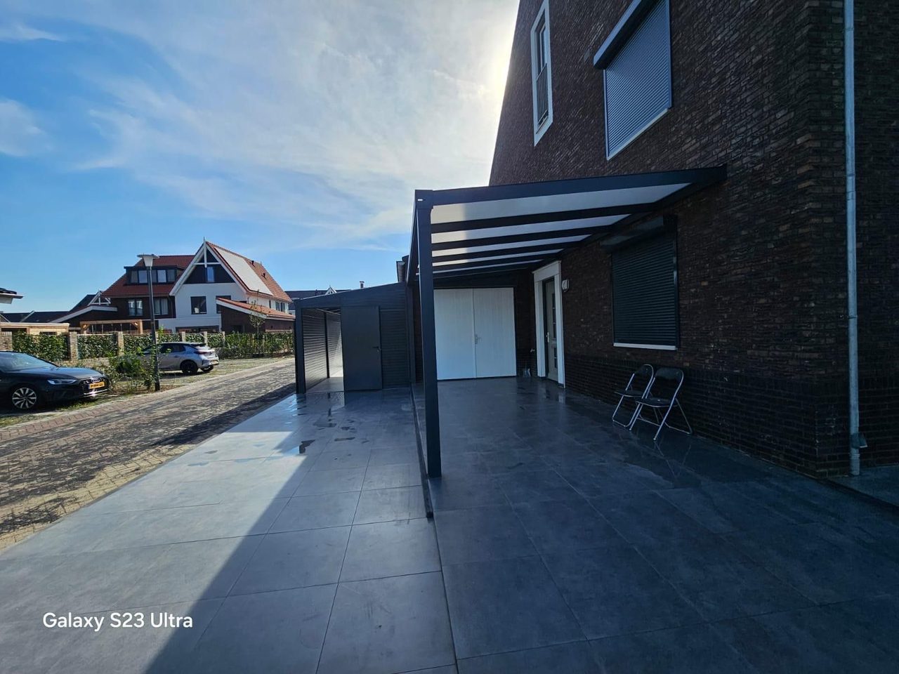 Terrasoverkapping aan een donkere bakstenen woning met antraciet tegels