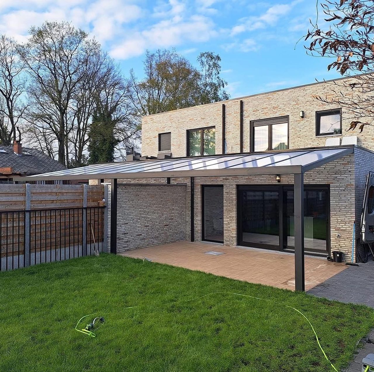 Terrasoverkapping met glazen dak aan een moderne woning met gazon