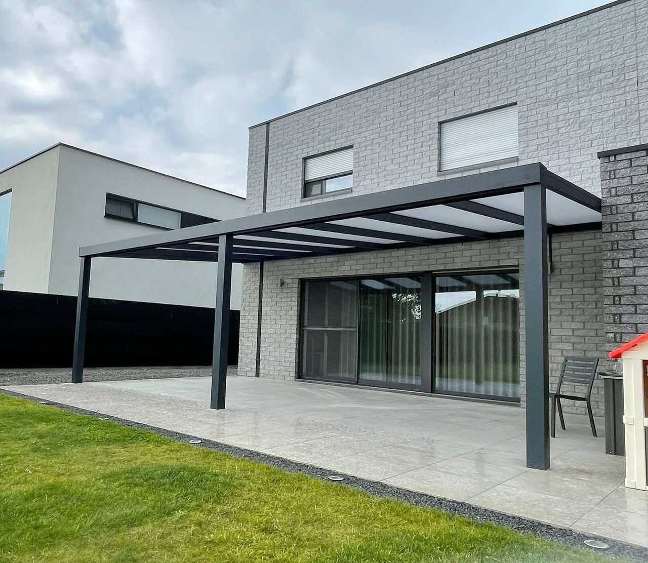 Terrasoverkapping aan een moderne grijze woning met tuinset