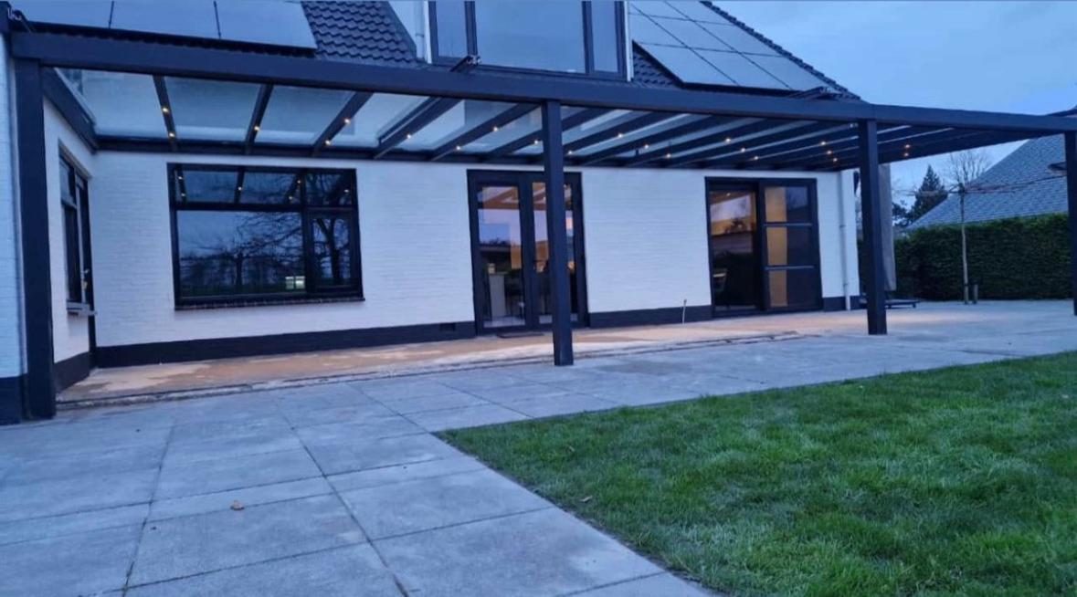 Brede terrasoverkapping met LED-spots aan een witte woning bij schemering