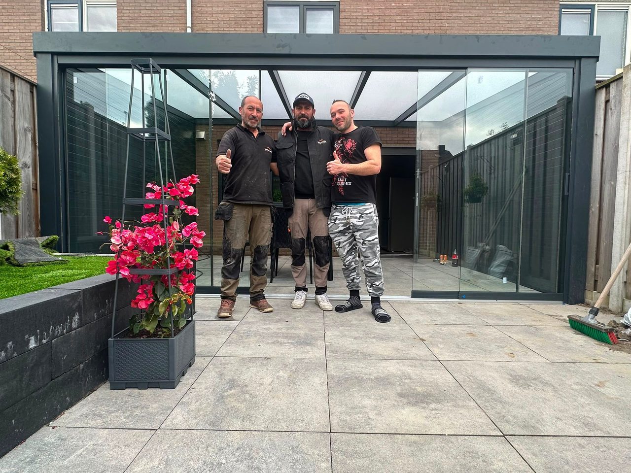 Drie montagemedewerkers bij een zojuist opgeleverde tuinkamer met glazen schuifwanden