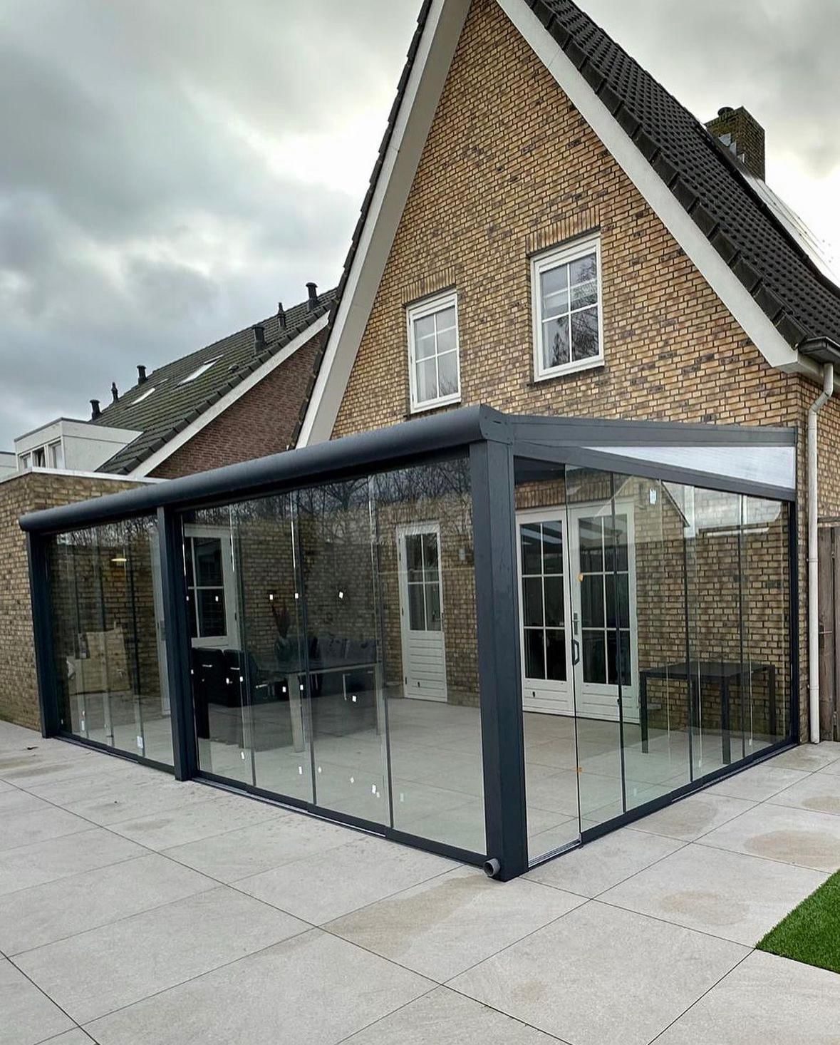 Hoektuinkamer met glazen schuifwanden aan een woning van gele baksteen