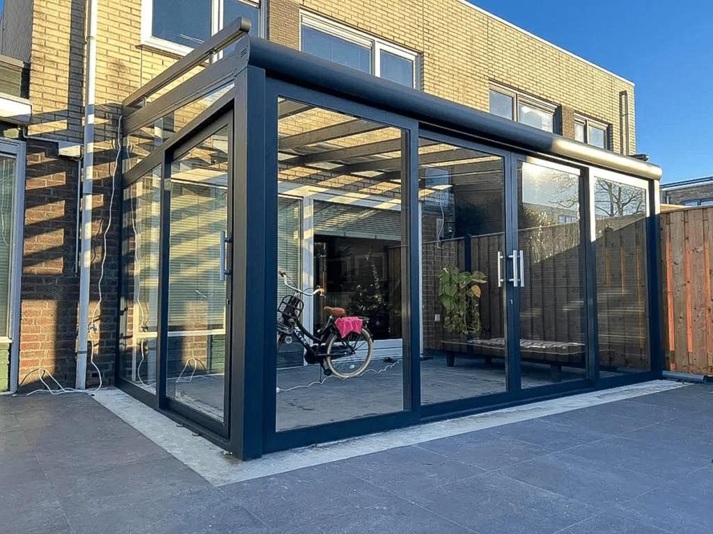 Tuinkamer met glazen schuifwanden aan een woning van gele baksteen