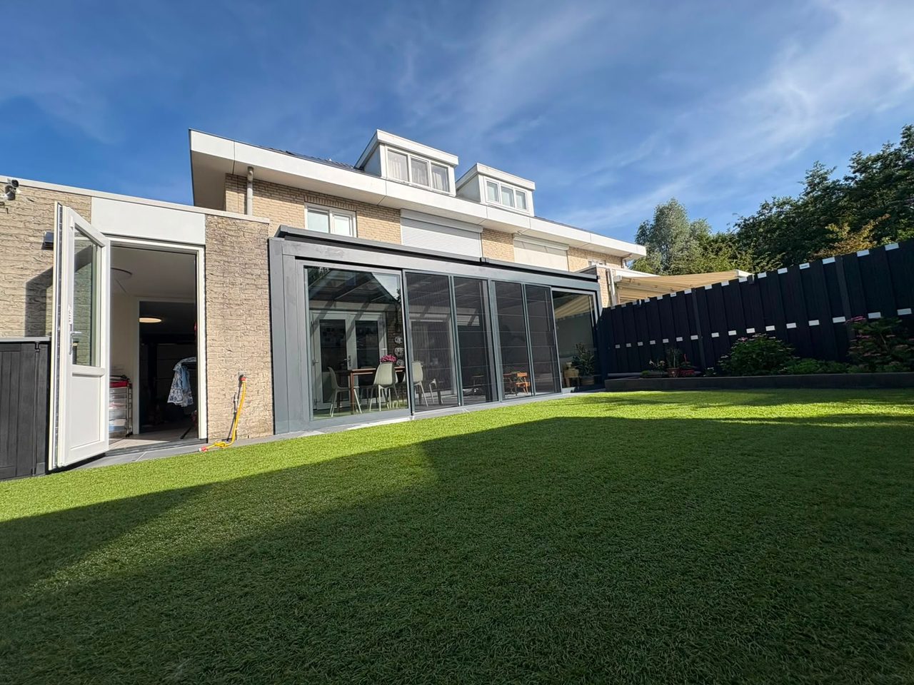 Brede tuinkamer met glazen schuifwanden aan een woning met ruim gazon