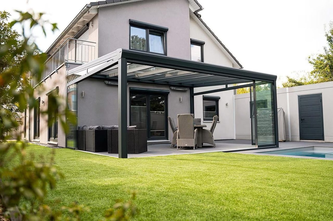 Veranda met glazen dak en glazen zijwand aan een moderne woning met gazon